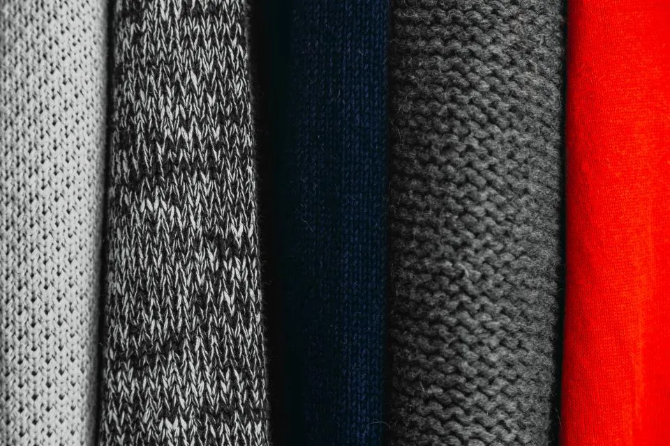 Folded knitwear in grey, navy and red showing the fine knit
